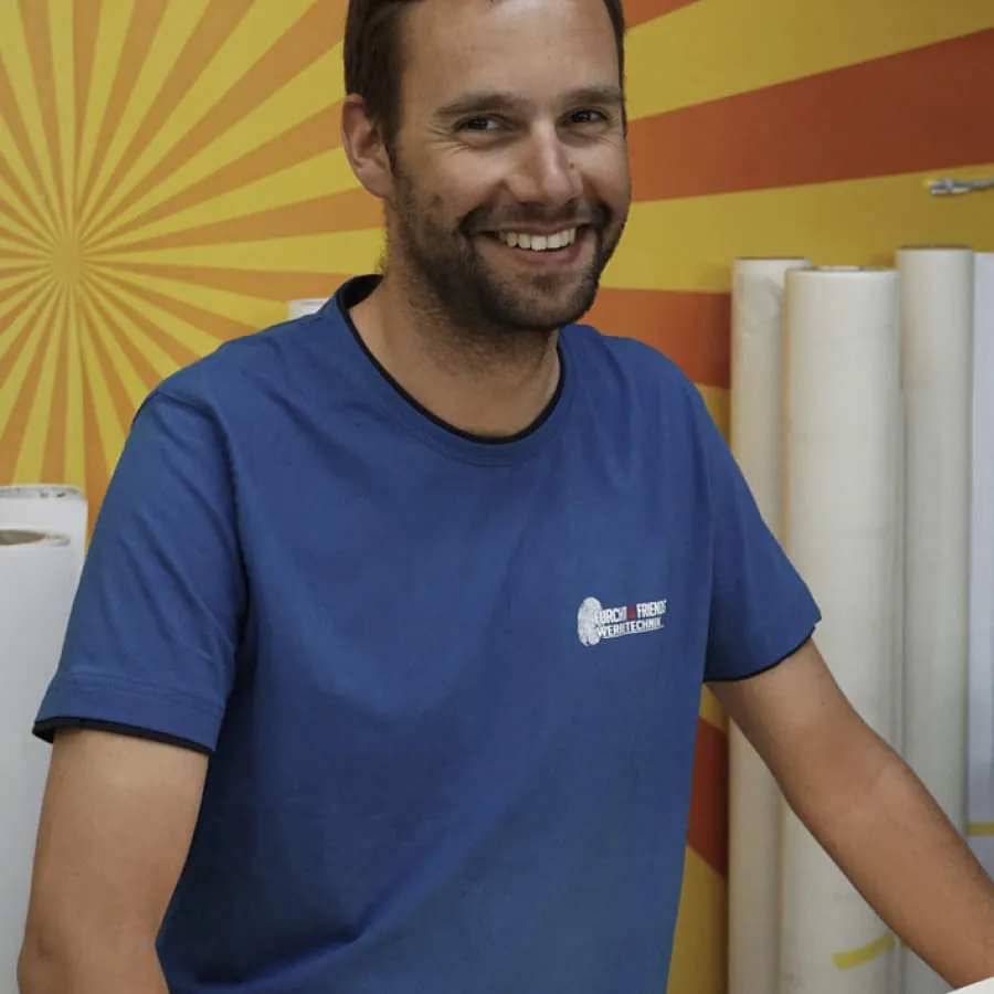 Mann in blauer T-Shirt vor orangefarbener Wand mit Strahlen