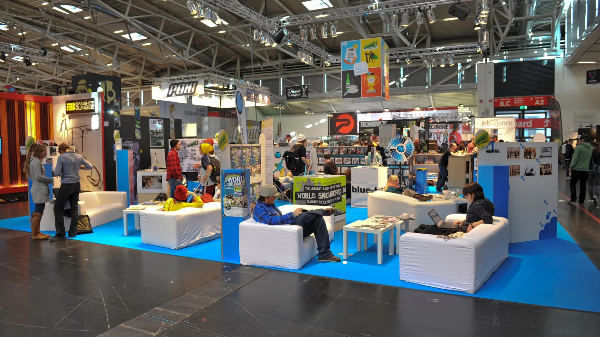 Messestand mit Sitzbereichen und Besuchern auf blauem Teppich