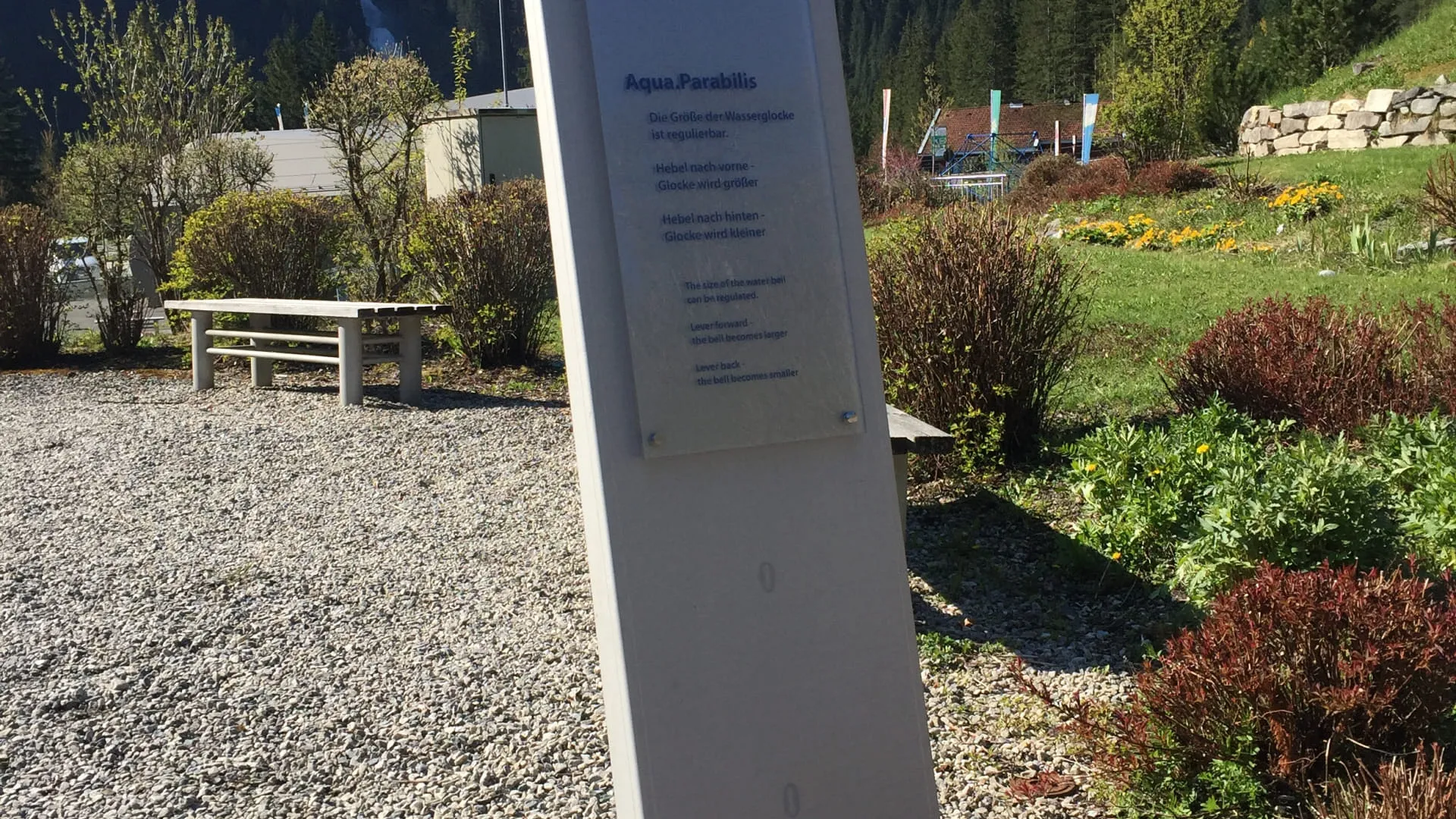Informationsschild in einer Landschaft mit Bergen und Blumenbeeten